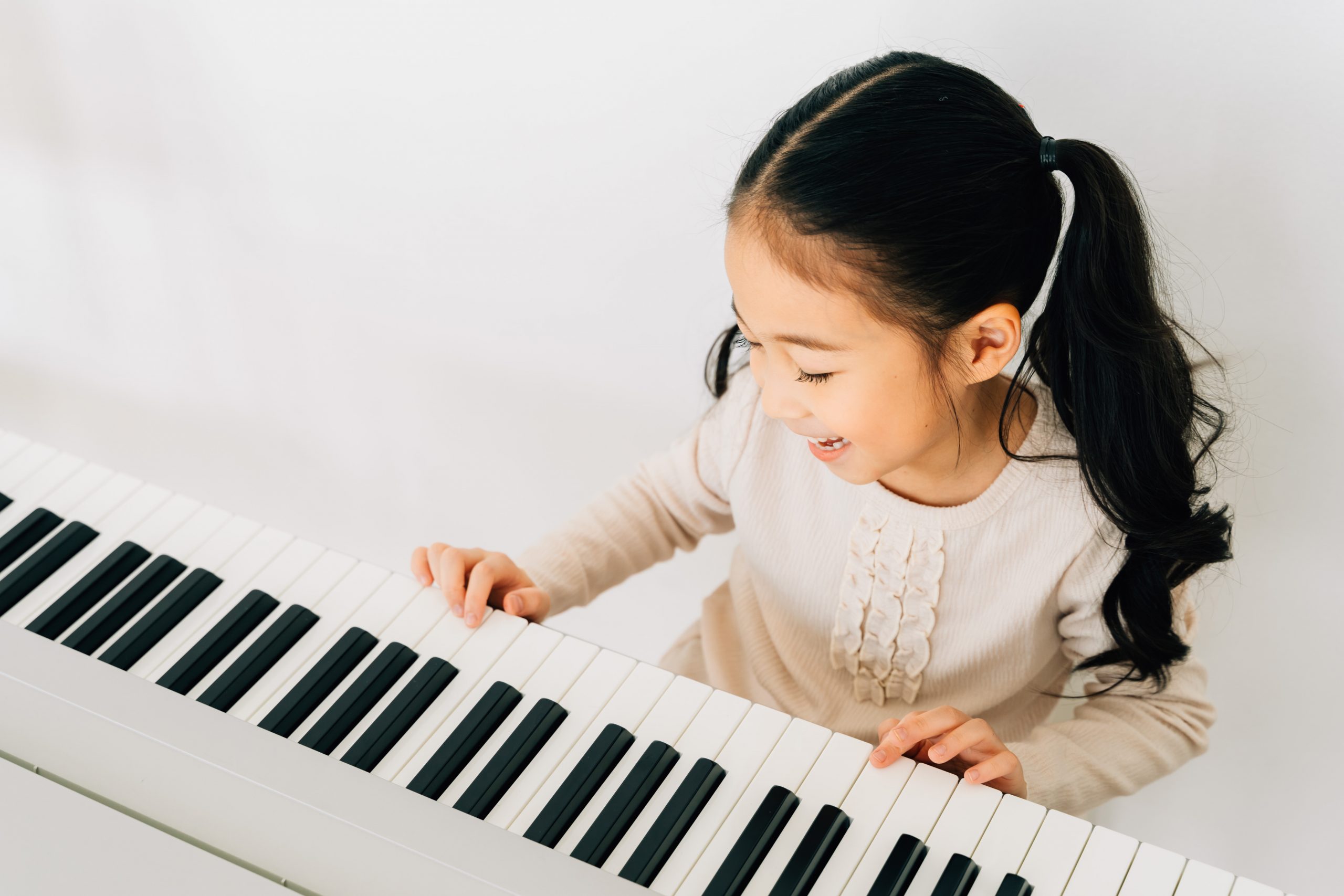 From above of happy smiling cute Asian girl playing piano enjoying time practicing music at home